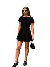 Woman in a black dress standing on a city street.