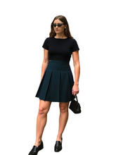 Woman in black top and green pleated skirt standing on a city street.
