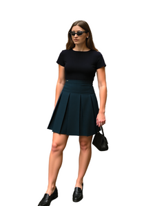 Woman in black top and green pleated skirt standing on a city street.