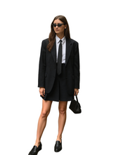 Woman in a black suit standing on a city street.