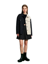Woman wearing a black coat over a white shirt, black skirt, and black boots on a green and white background
