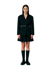 Woman wearing a black outfit with a belt and knee-high boots on a plain background