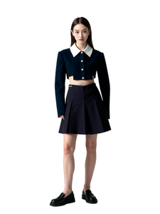 Woman wearing a black cropped jacket and pleated skirt on a light gray background