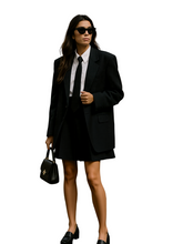 Woman in a black suit and sunglasses standing on a street.