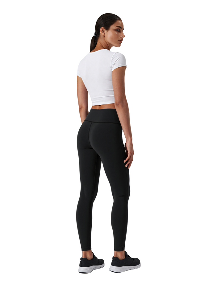 Woman wearing black leggings and a white crop top on a white background