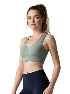 Woman wearing a green sports bra and navy leggings on a light gray background