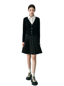 Person wearing a black cardigan, white shirt, and black skirt on a plain background