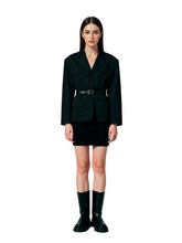 Woman wearing a black blazer and skirt set with black boots on a white background