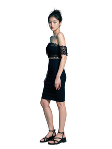Woman in a black outfit standing on a stool against a light blue background
