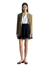 Woman wearing a brown blazer, white shirt, and black skirt on a white background