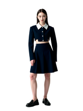 Woman wearing a navy blue outfit with a white collar on a light gray background