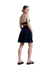 Woman wearing a black strapless top and navy skirt against a gray background
